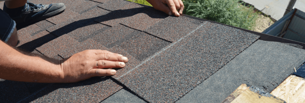 Close up picture of expert hands laying roofing materials on a roof.
